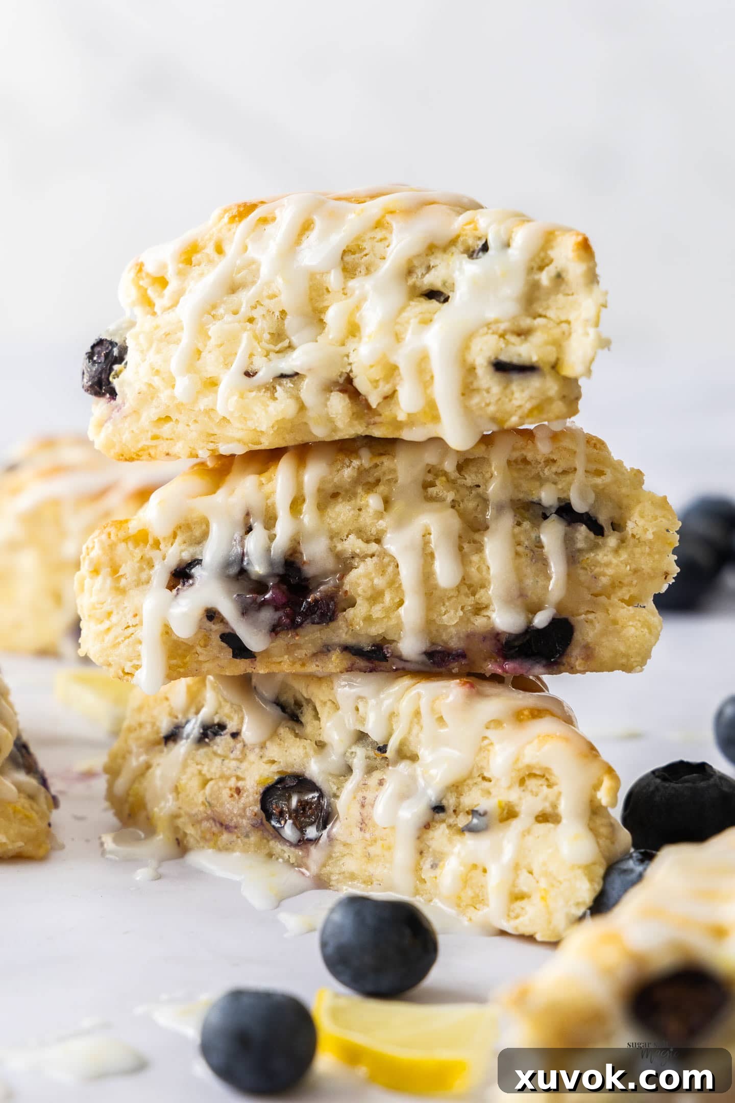 A stack of 3 fluffy blueberry and lemon scones with a sweet glaze drizzling down the sides.