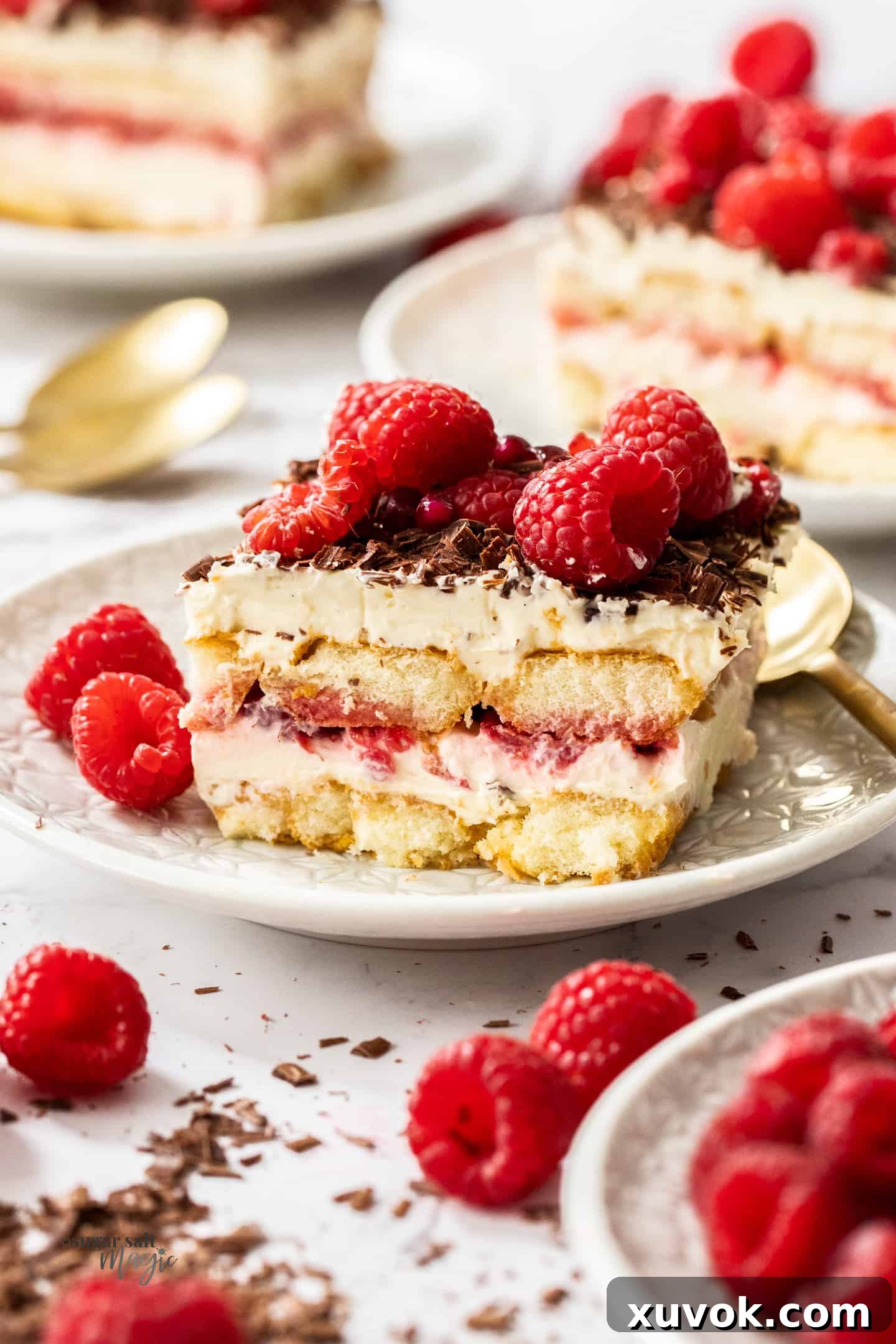 A slice of raspberry tiramisu on a white plate surrounded by fresh raspberries.