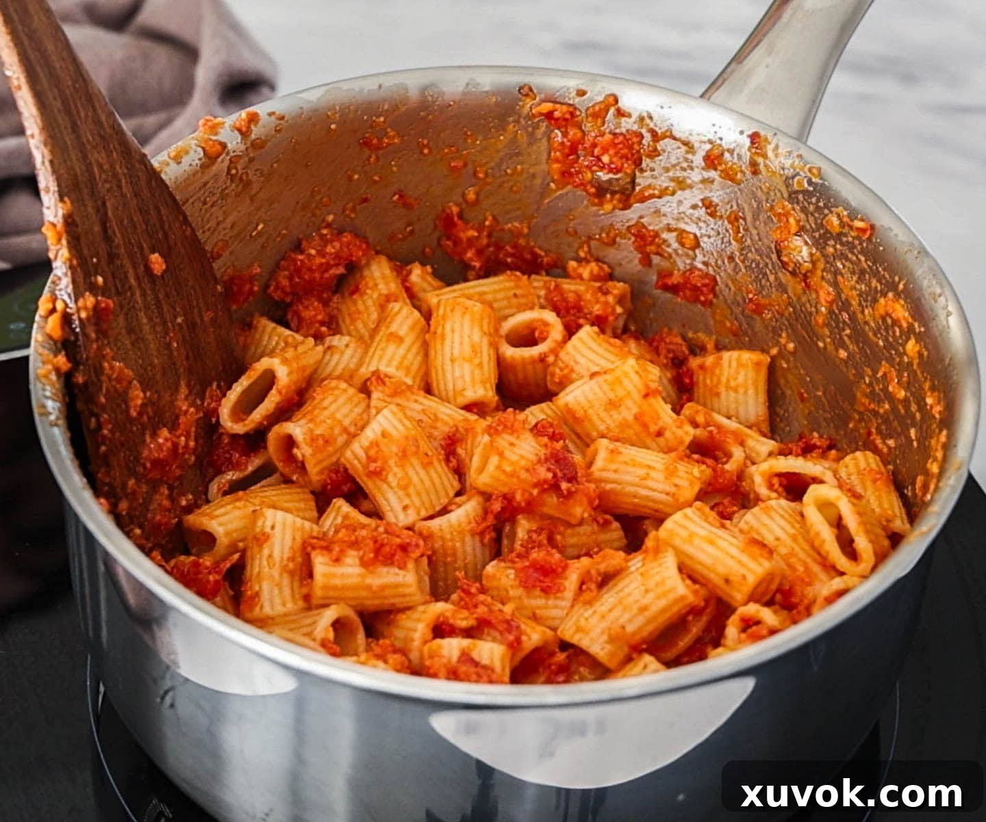 Pasta in a saucepan, mixed with sundried tomato pesto.